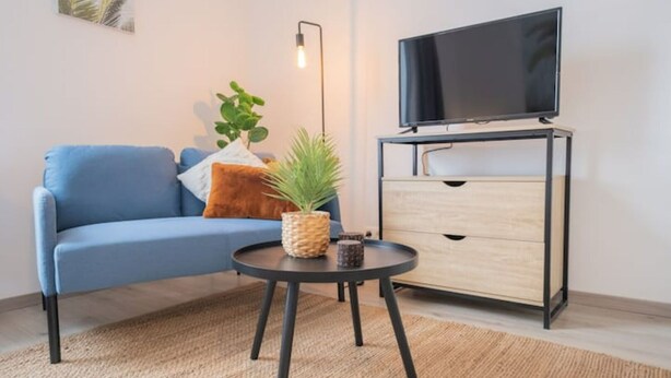 Un soggiorno moderno con un divano blu, un tavolino rotondo con una pianta, una TV su un mobile basso e un armadietto in legno.