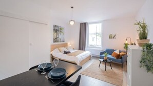 Una camera d'albergo moderna con un letto, un tavolo da pranzo con piatti e bicchieri, un divano blu e un piccolo tavolino con una pianta.