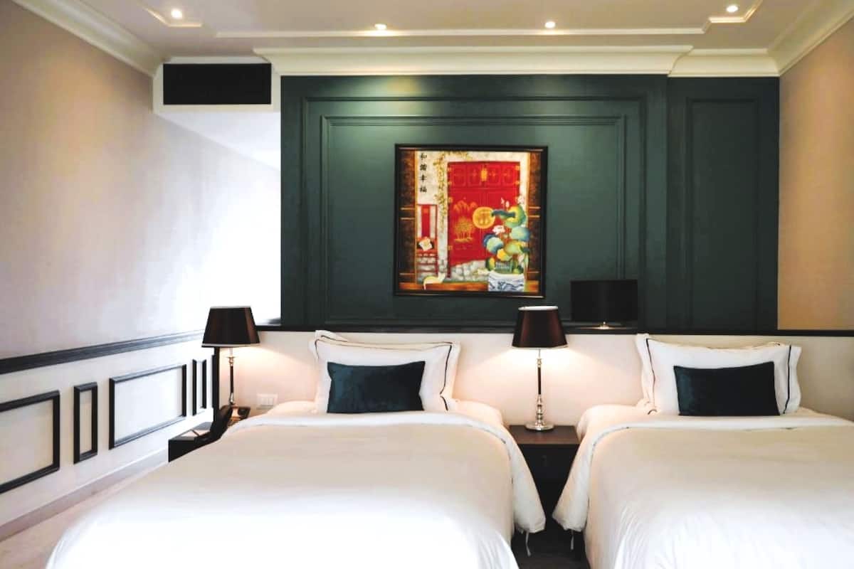 A hotel room with two beds, a large painting on the wall, and two lamps.