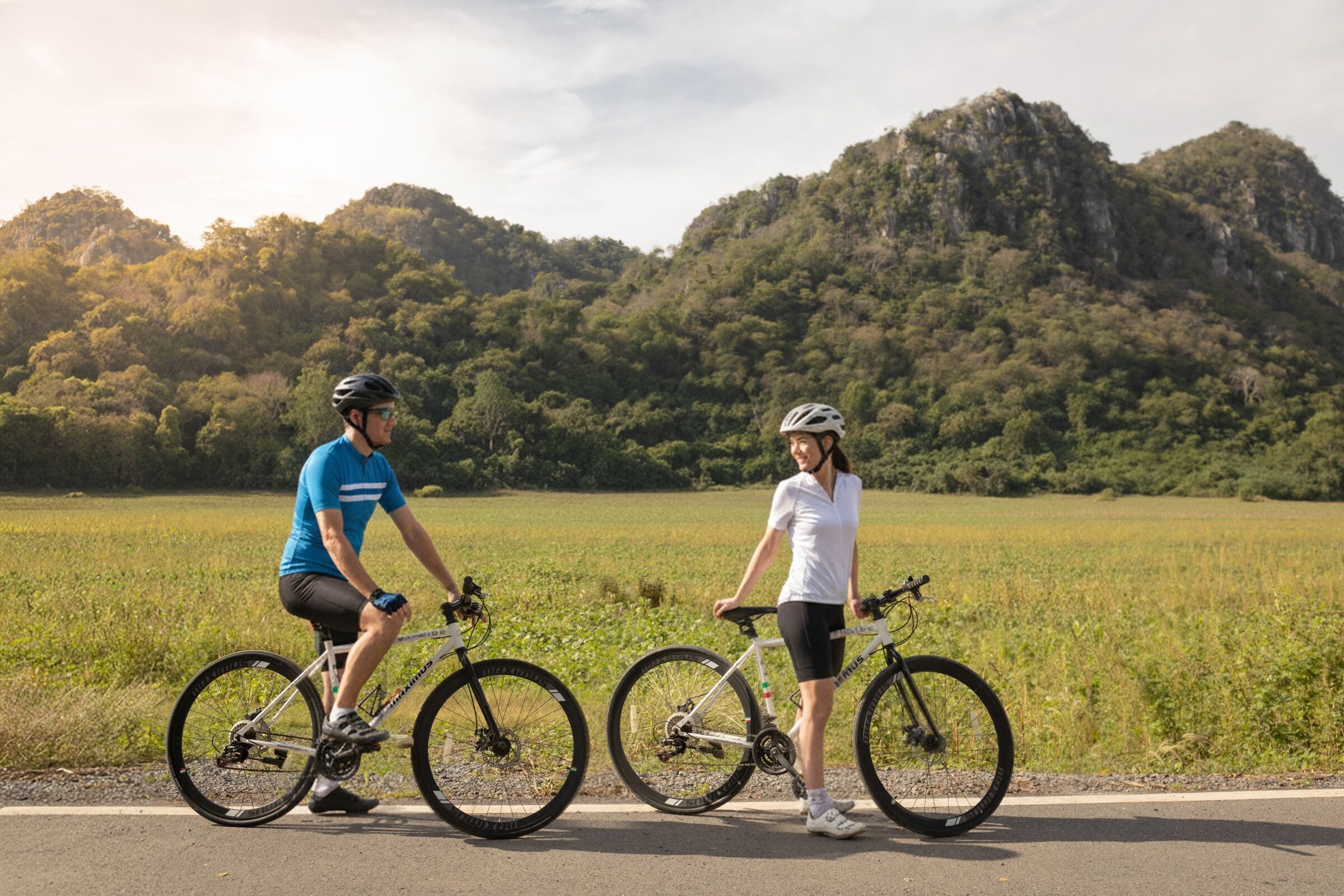 Two cyclists on a road with a mountainous backdrop.