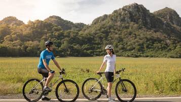 Two cyclists on a road with a mountainous backdrop.