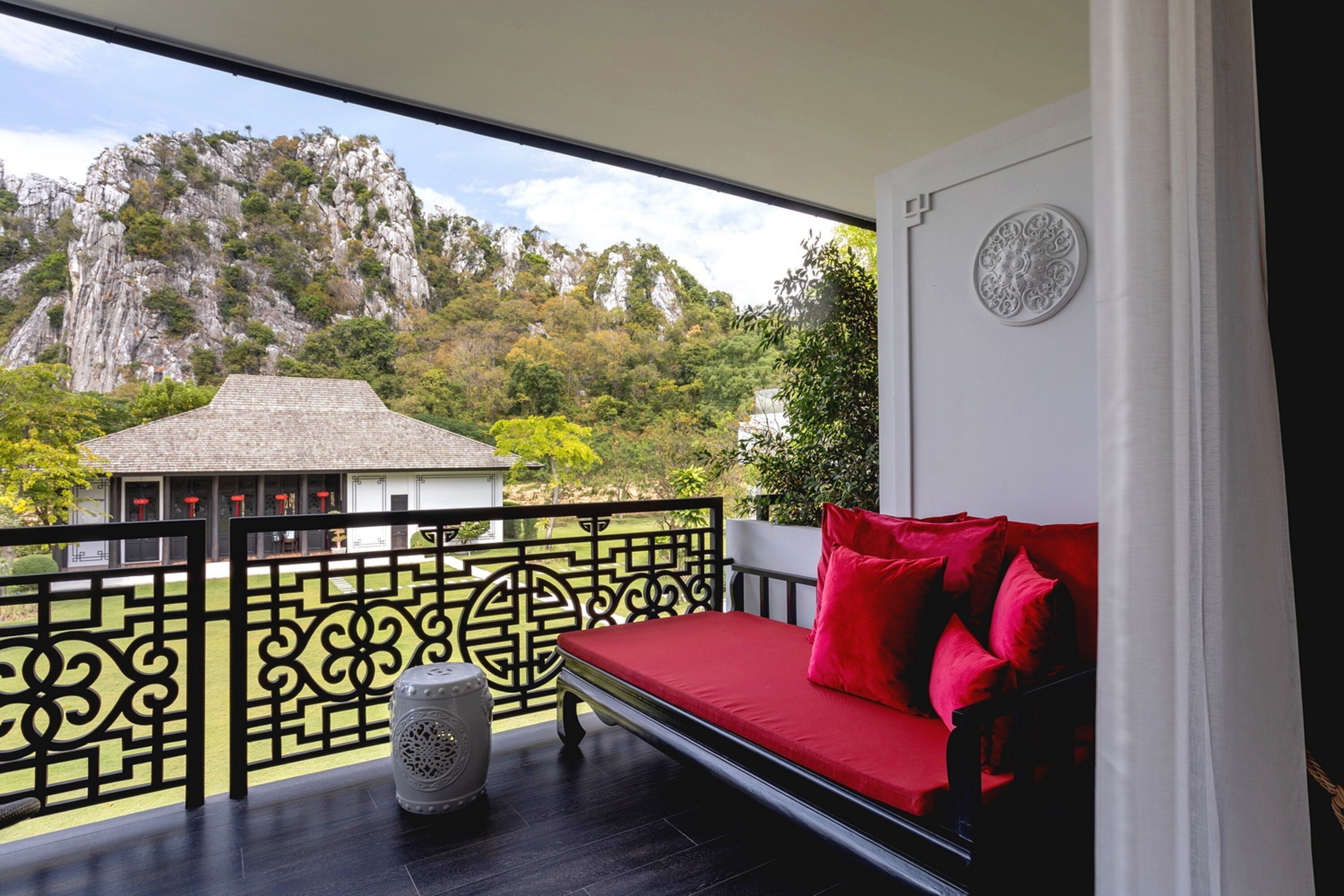 Uma varanda com um sofá vermelho, um vaso decorativo e vista para uma montanha.