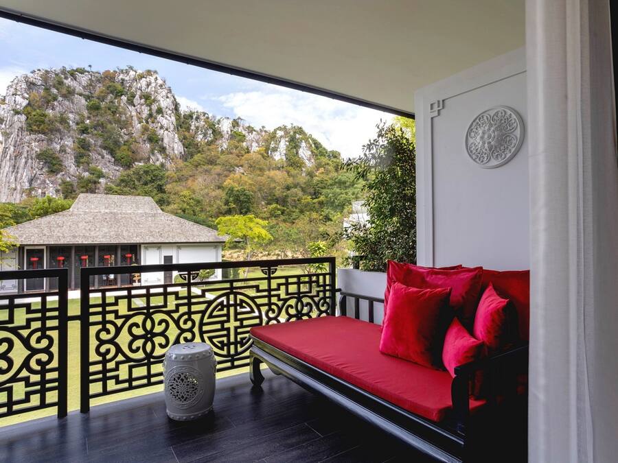 A balcony with a red sofa, a decorative vase, and a view of a mountain.