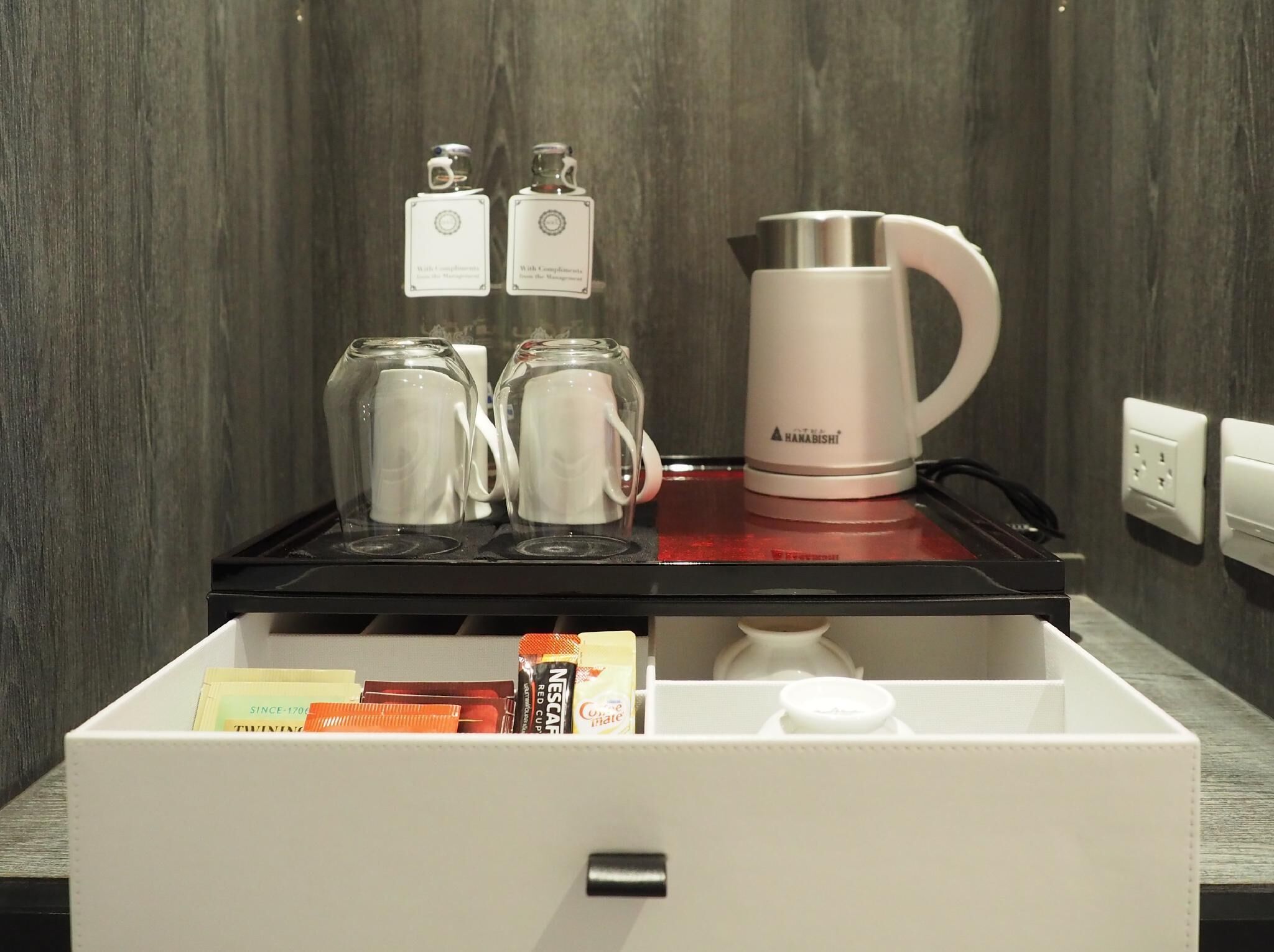 A kitchen area with a coffee maker, two glass mugs, and a drawer containing coffee pods and a bottle.