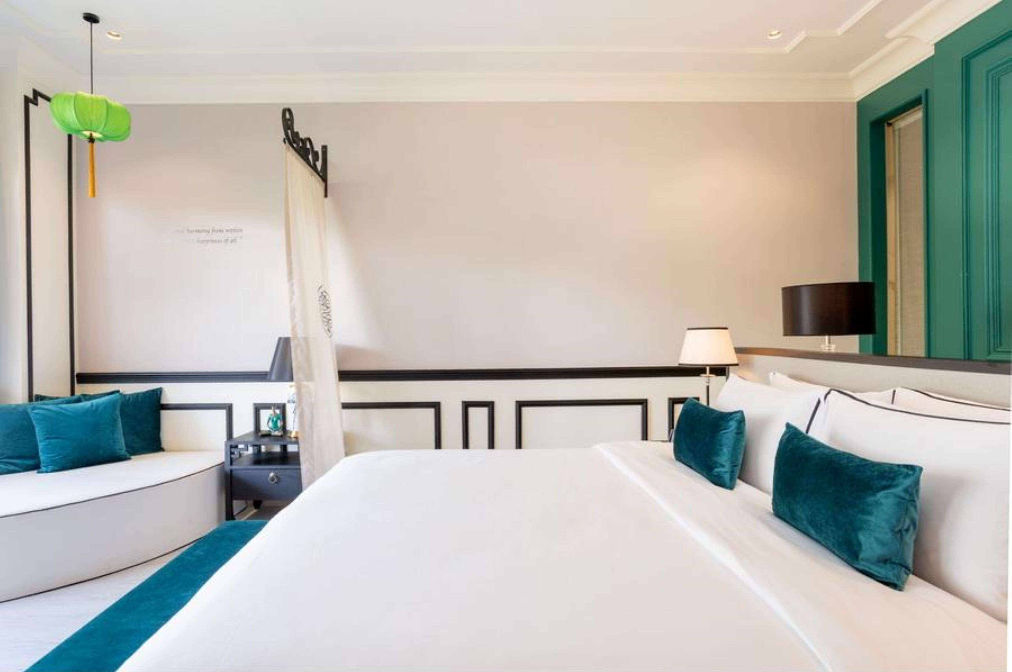 A modern hotel room with a large bed, a curved seating area, a desk, and a green accent wall.