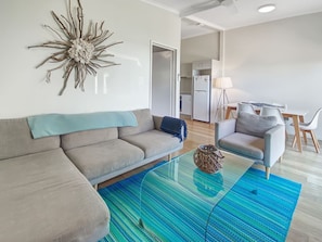 A modern living room with a sofa, a glass coffee table, a decorative wall piece, and a dining area with chairs and a table.