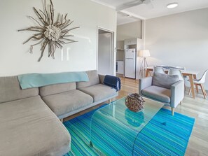 Un salon moderne comprenant un canapé, une table basse en verre, un élément décoratif mural et un coin repas avec des chaises et une table.