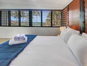 A hotel room with a bed, a blue blanket, and a view of palm trees through the window.