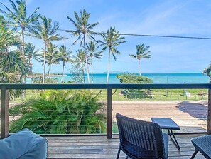 Un balcon avec vue sur l’océan, des palmiers et une zone verdoyante.