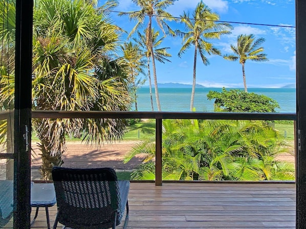 A balcony with a view of palm trees and the ocean.