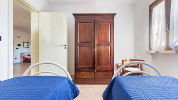A bedroom with two beds, a wardrobe, and a window with curtains.