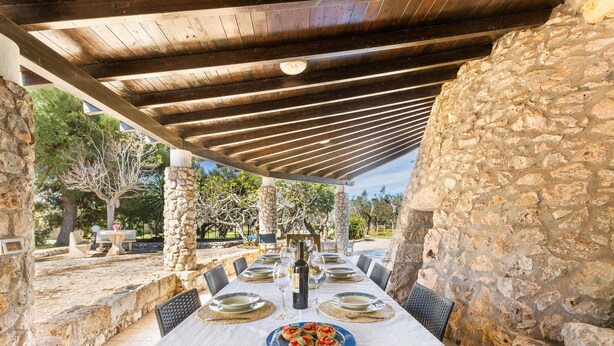 An outdoor dining area with stone walls, a wooden pergola, and a table set for a meal.
