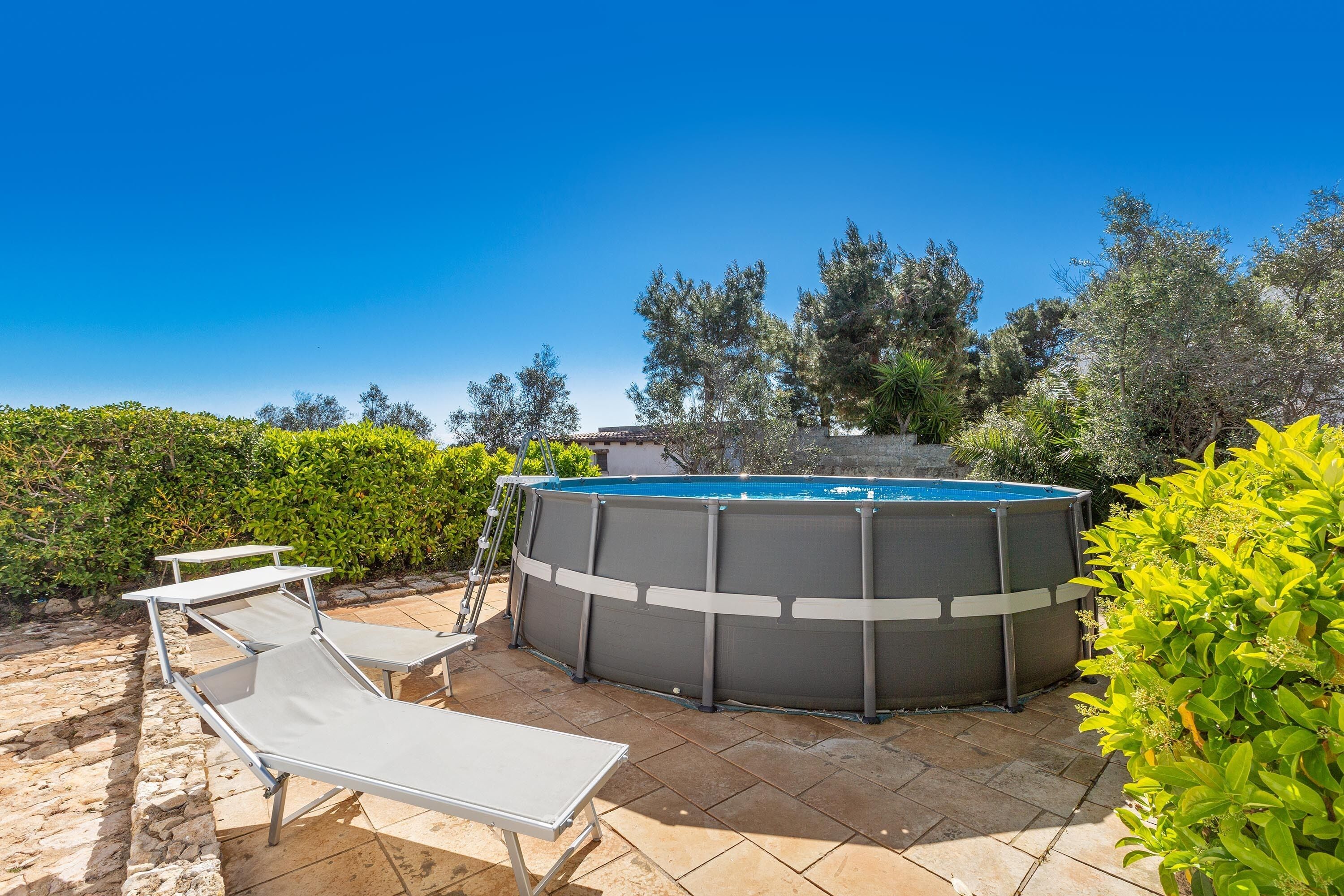 A swimming pool with lounge chairs and a ladder, surrounded by greenery.