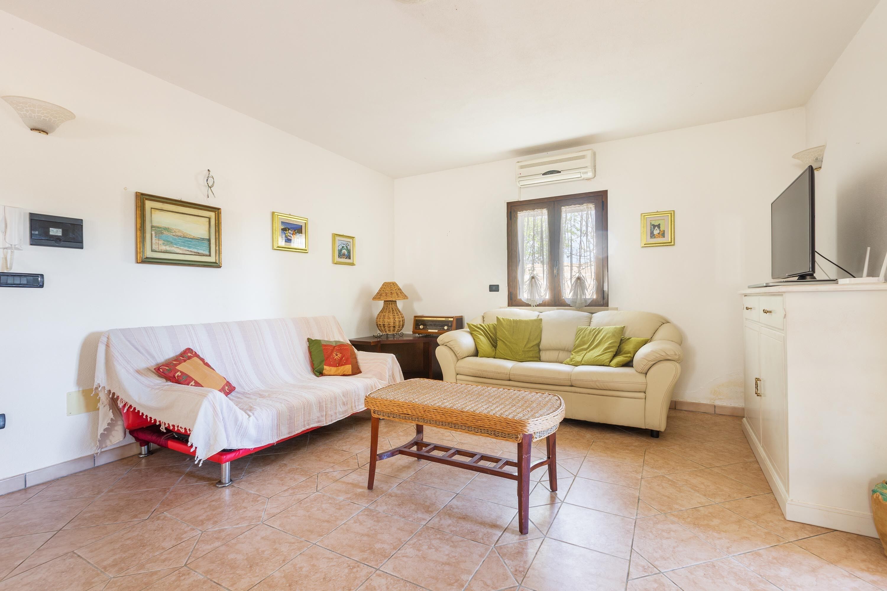 A living room with a red sofa, a beige sofa, a wicker coffee table, and a television on a cabinet.