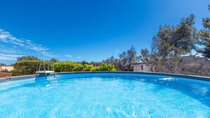 A clear blue swimming pool with a ladder, surrounded by greenery and a stone wall.