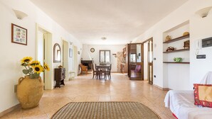 A spacious living area with a dining table and chairs, a large vase with sunflowers, and a bed with a red pillow.