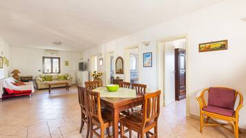 A spacious living area with a dining table, chairs, a sofa, and a wicker chair.