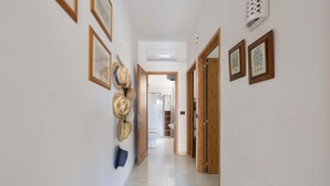 Un couloir avec des tableaux encadrés accrochés aux murs, un ventilateur de plafond et une porte donnant sur une autre pièce.