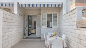 Une petite terrasse extérieure avec une table et des chaises, une porte donnant sur une pièce intérieure et un mur en pierre.