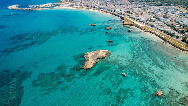 Vue aérienne d’une ville côtière, avec ses eaux turquoise limpides, sa plage de sable et un ensemble dense de bâtiments le long de la côte.