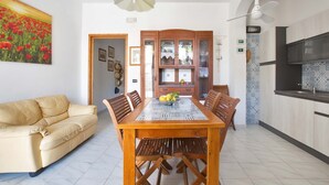 Un coin repas avec une table et des chaises en bois, un canapé beige et une cuisine dont le mur derrière l’évier est recouvert de carreaux.