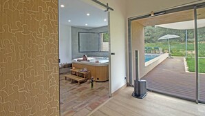 A modern bathroom with a wooden puzzle pattern wall, a hot tub, and a view of an outdoor deck with a pool.