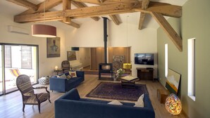 A spacious living room with wooden beams, a fireplace, a television, and comfortable seating.