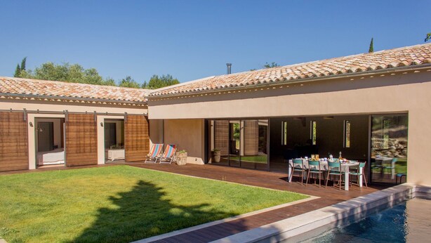 A modern house with a swimming pool, a patio with a table and chairs, and a well-maintained lawn.