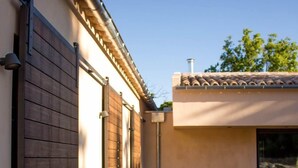 A narrow wooden pathway leading to a modern building with a tiled roof and a large sliding door.