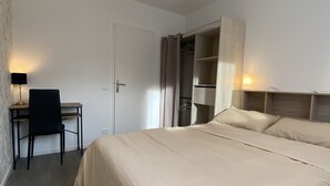 A hotel room with a large bed, a desk with a chair, a wardrobe, and a hanging light fixture.