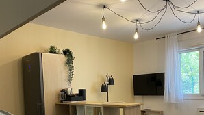 A compact kitchen with a built-in refrigerator, wooden shelves, a dining area with a table and chairs, and a TV mounted on the wall.