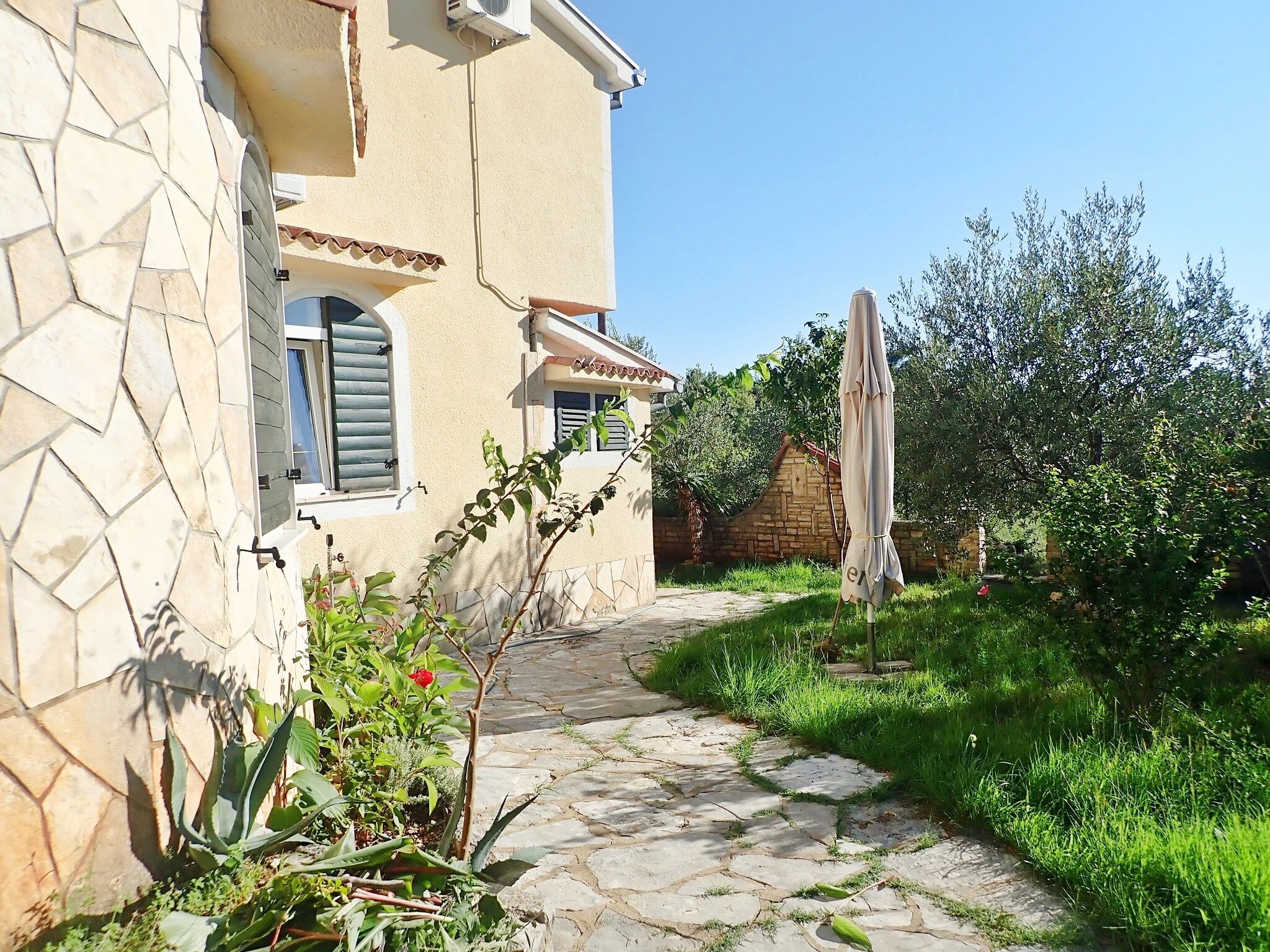 A stone pathway leading to a building with a tiled roof and a window with shutters.