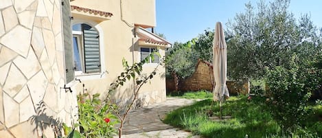 A stone pathway leading to a building with a tiled roof and a window with shutters.