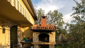 Eine Terrasse im Freien mit einem gemauerten Pizzaofen, Holzbänken und einem Fliesenboden.