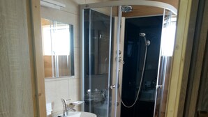 Uma casa de banho moderna com chuveiro envidraçado, lavatório branco e toucador de madeira.
