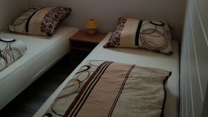 Acomodação compacta, com um quarto e duas camas de solteiro, uma pequena mesa com abajur e janela com cortinas.