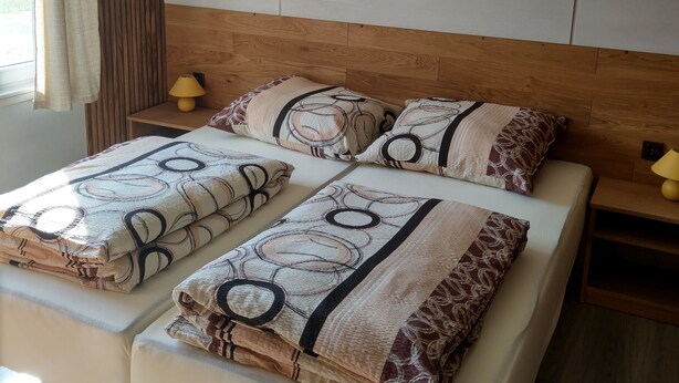 Uma cama de casal com roupa de cama estampada, cabeceira de madeira e mesa de cabeceira com abajur.
