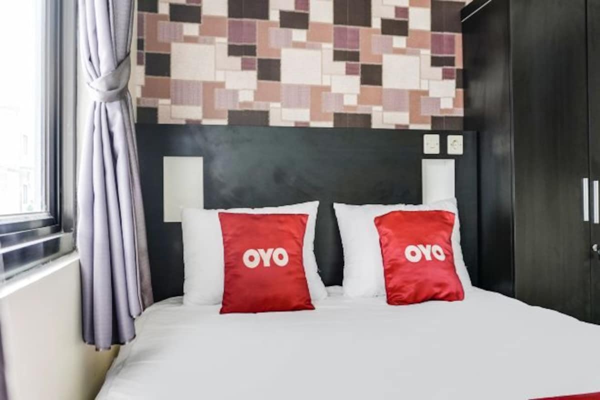 Een hotelkamer met een bed, twee rode kussens met 'OYO'-branding, een donker hoofdeinde en een muur met een gepixelde print.
