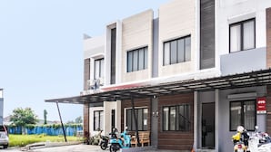 Een modern gebouw met een overdekte ingang, een blauwe scooter en een motorfiets voor de deur.