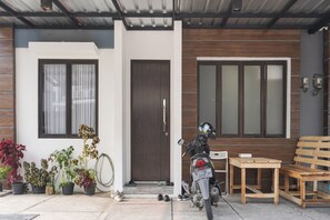 A modern house with a motorcycle parked in front, a wooden bench, and potted plants.