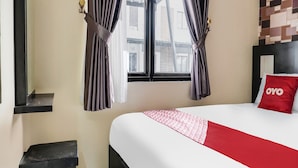 Hotelkamer met een bed, nachtkastje, raam met gordijnen en wand met een geometrisch patroon.