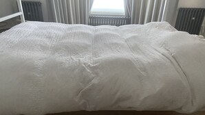 Ein Bett mit weißer Daunendecke in einem Zimmer mit Holzboden und Meerblick durch ein mit Vorhängen versehenes Fenster.