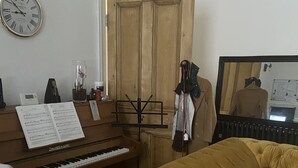 Ein Zimmer mit Klavier, einer Couch, einem Spiegel und einer Wanduhr.