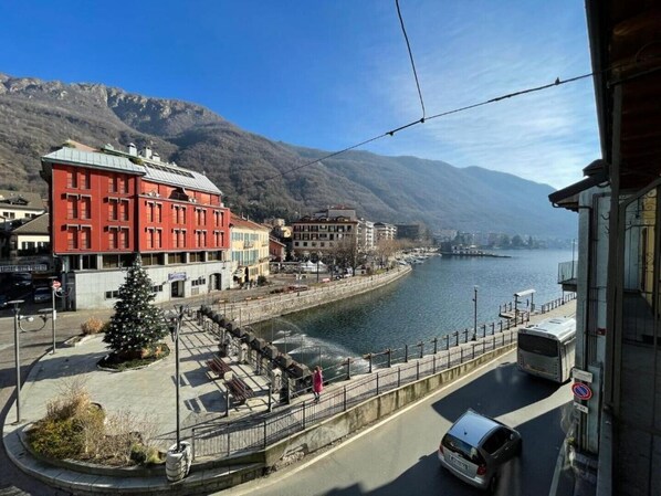 A waterfront view with a red building, a pedestrian walkway, and a road with a bus.
