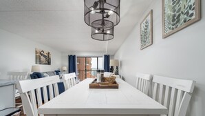 Uma área de refeições com mesa e cadeiras brancas, um candelabro e obras de arte nas paredes.