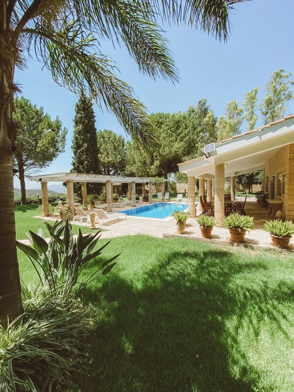 A pool area with a covered patio, potted plants, and a clear sky.