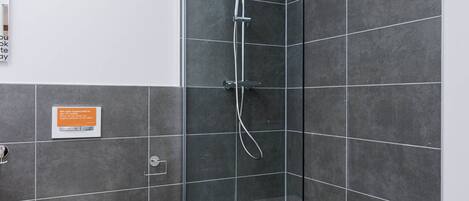 Un baño moderno con ducha de vidrio, inodoro blanco y un estante pequeño con botellas.