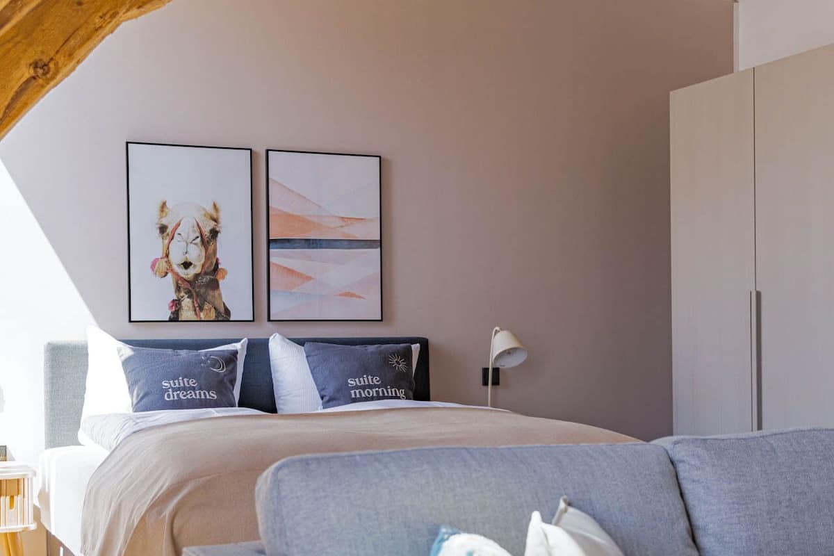Une chambre à coucher avec un lit, un canapé et un plafond avec des poutres apparentes. Deux tableaux encadrés sont accrochés au mur.