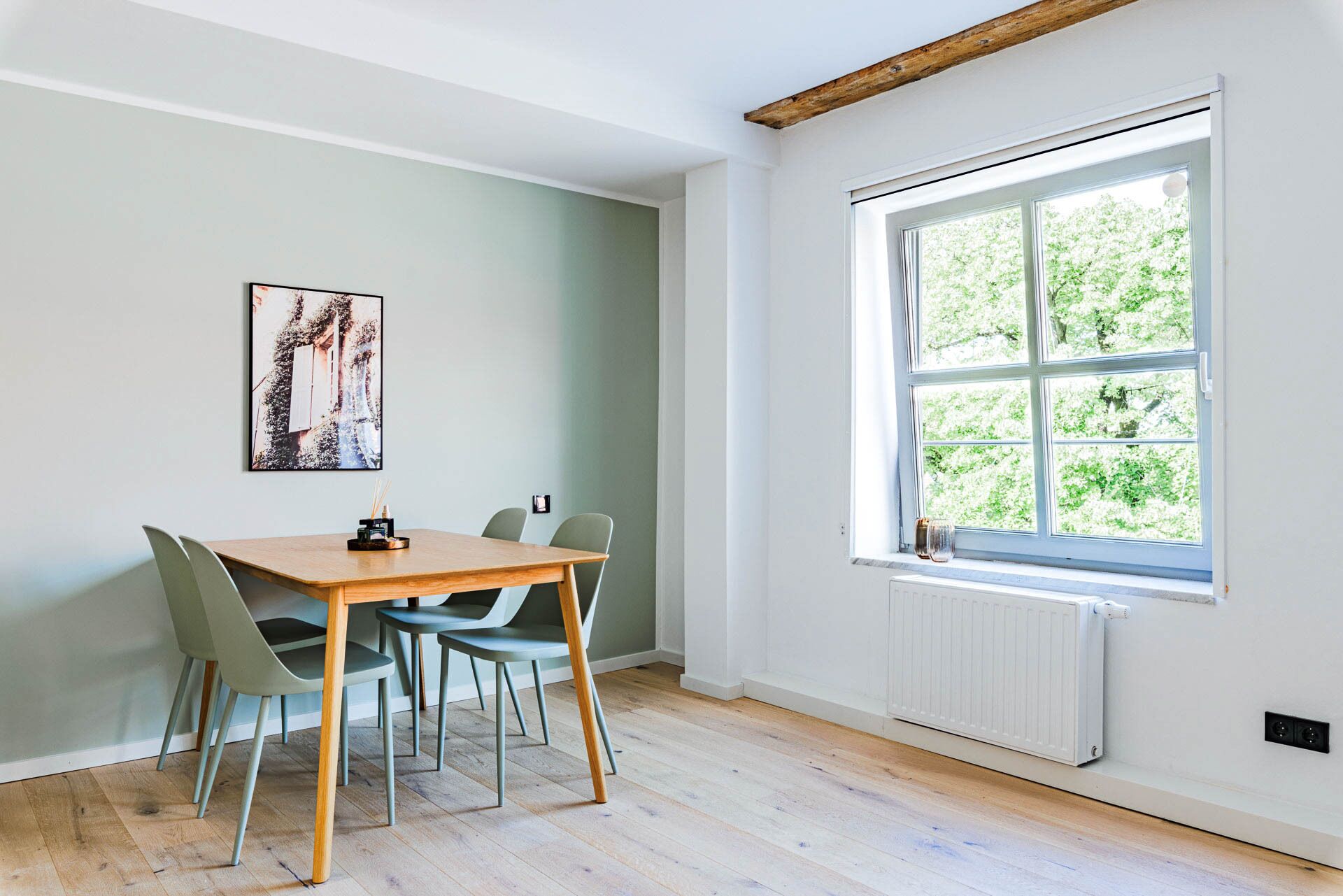Un comedor con una mesa de madera y cuatro sillas, un radiador y una ventana con vistas a zonas verdes.