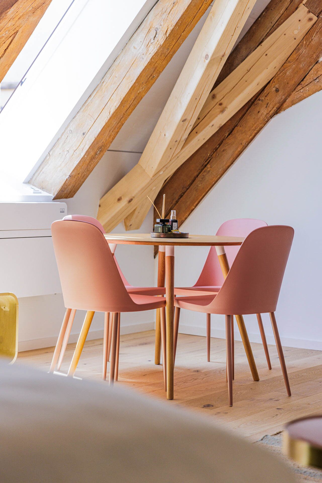 Un comedor con una mesa de madera y sillas rosadas, bajo un techo inclinado con vigas a la vista.